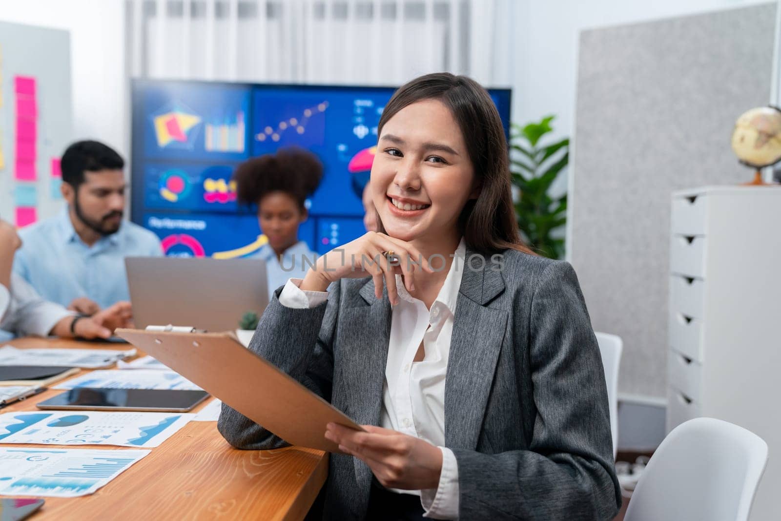 Portrait of happy young asian businesswoman with group of office worker on meeting with screen display business dashboard in background. Confident office lady at team meeting. Concord