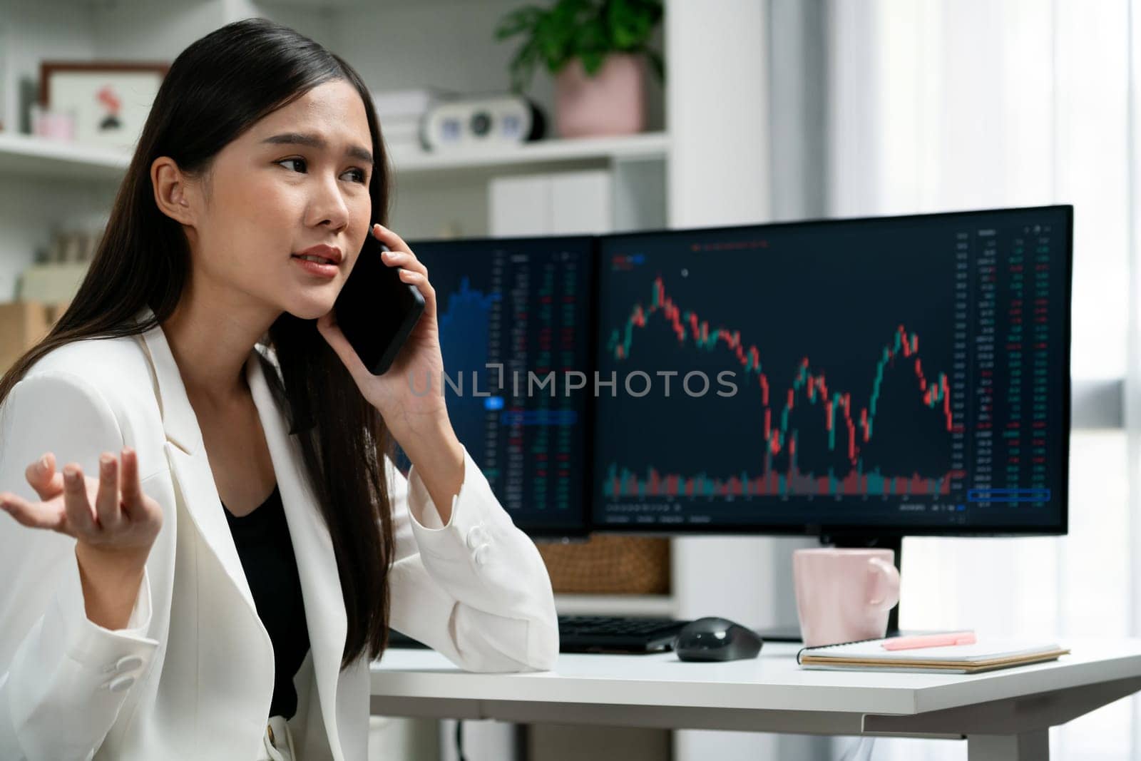 Stressful young beautiful Asian businesswoman calling to broker on smartphone, analyze possible risk to profit or loss in dynamic exchange stock market graph on pc screen at modern office. Stratagem.