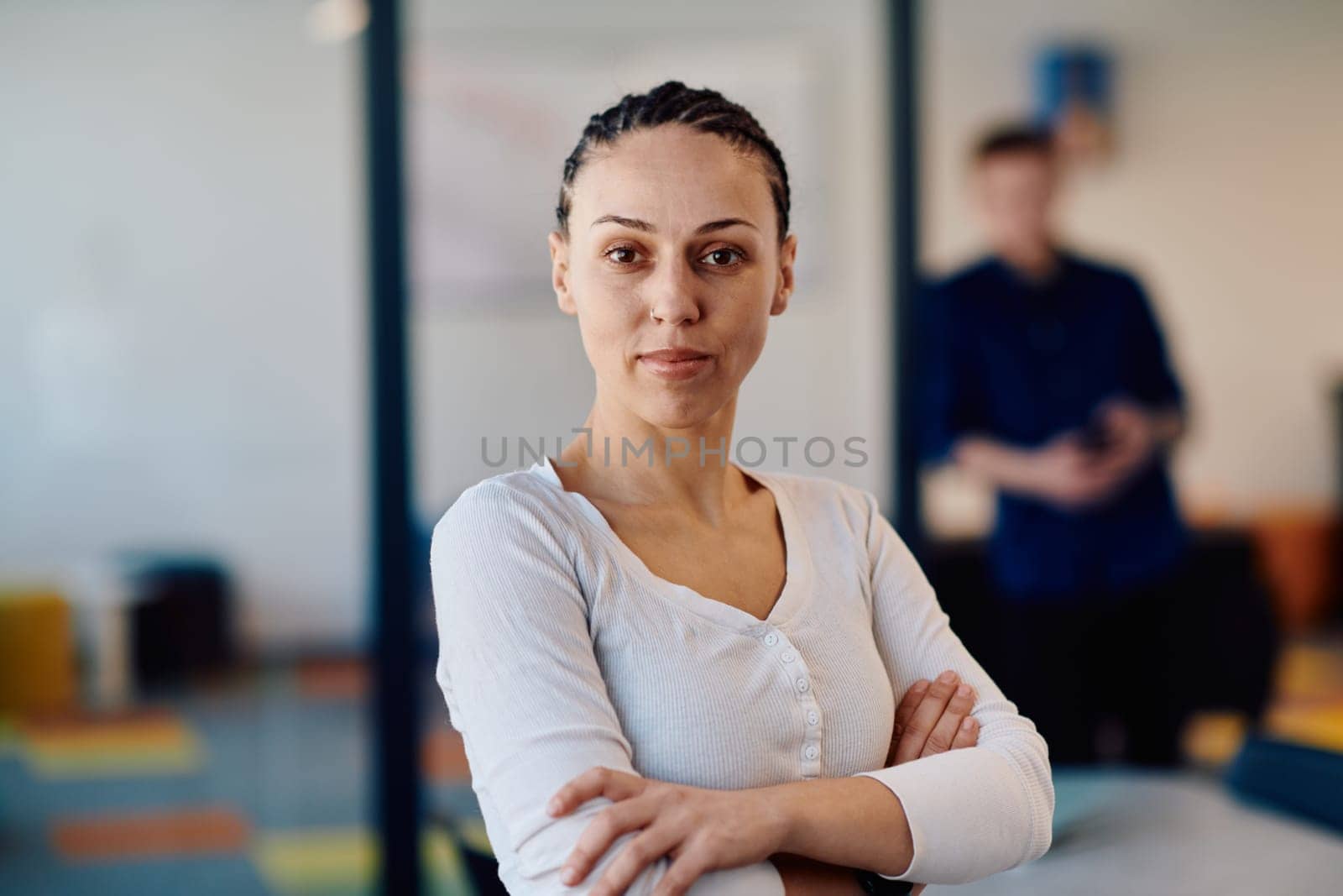 Portrait of a business woman in a creative open space coworking startup office with crossed arms. Successful businesswoman standing in office with copyspace. Associates work in the background by dotshock