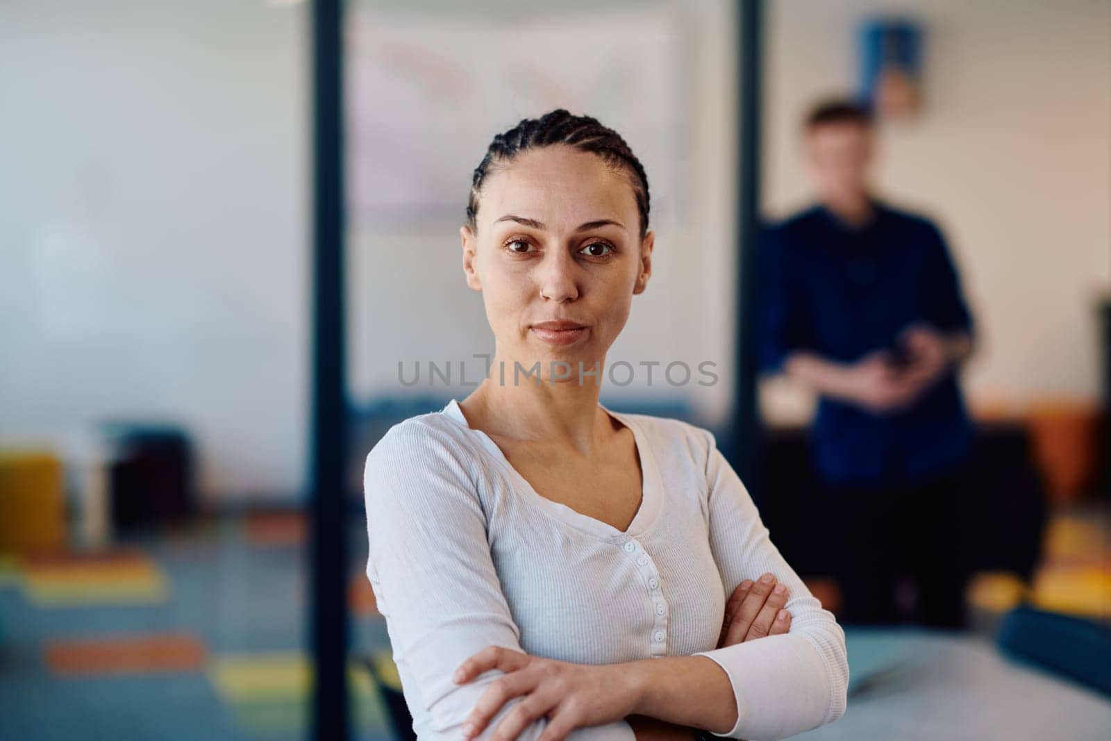 Portrait of a business woman in a creative open space coworking startup office with crossed arms. Successful businesswoman standing in office with copyspace. Associates work in the background.