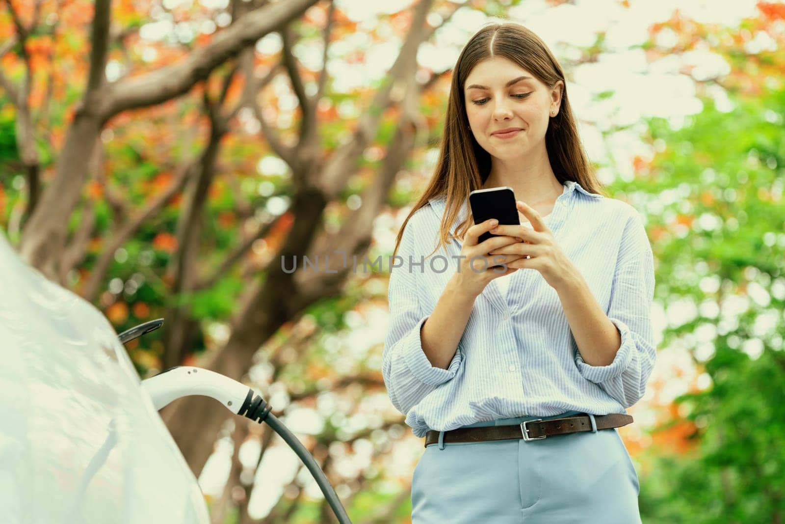 Young woman using smartphone to pay for electric car charging. Exalt by biancoblue