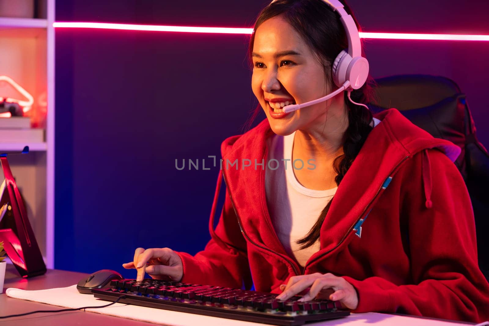 Host channel of smiling beautiful Asian girl streamer playing online game wearing headphone talking with viewers media online recording phone. Esport skilled team players in neon blue room. Stratagem.