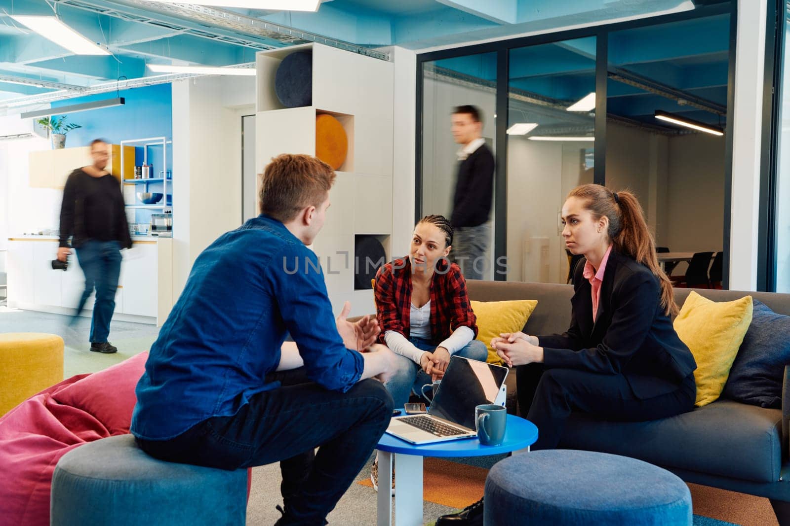 Multiethnic startup business team on meeting in a modern bright open space coworking office. Brainstorming, working on laptop. Group of coworkers walking around in motion blur.