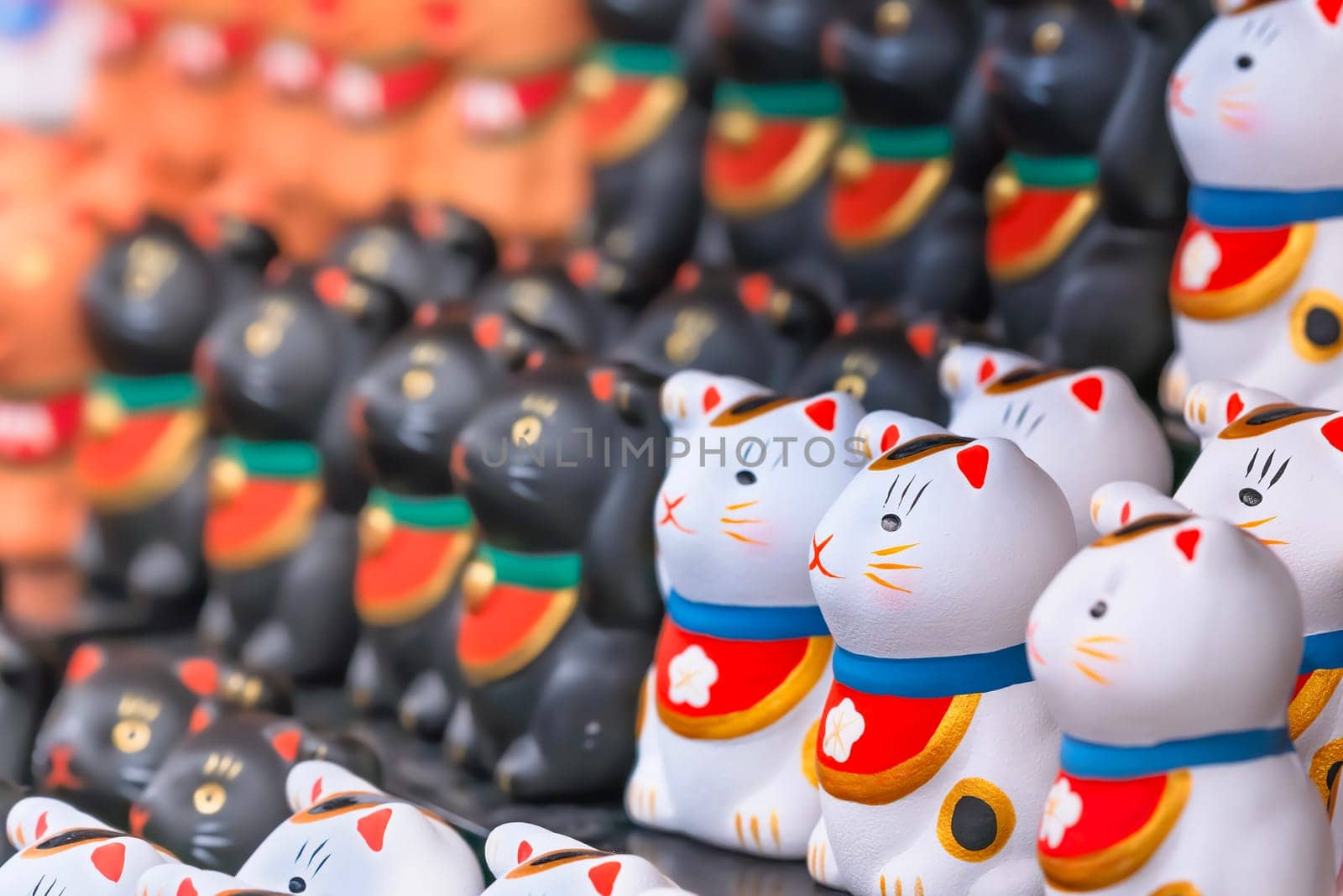 A bunch of aligned tiny and adorable stylized hand painted white Japanese manekineko cats lucky charm sculptures depicting to the famous beckoning cat and wearing bib adorned with a cherry blossom.