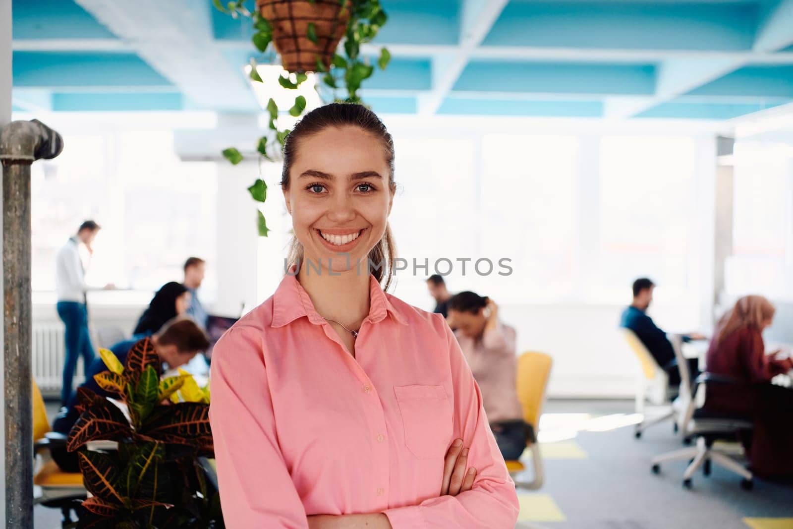 Portrait of young smiling business woman in creative open space coworking startup office. Successful businesswoman standing in office with copyspace. Coworkers working in background.