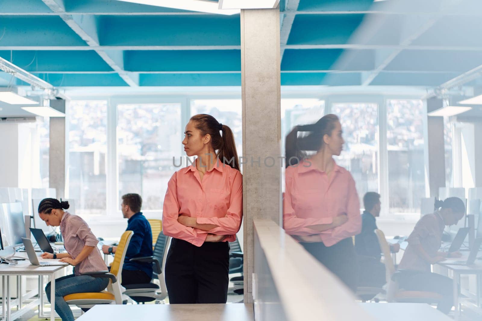 Portrait of young smiling business woman in creative open space coworking startup office. Successful businesswoman standing in office with copyspace. Coworkers working in background.