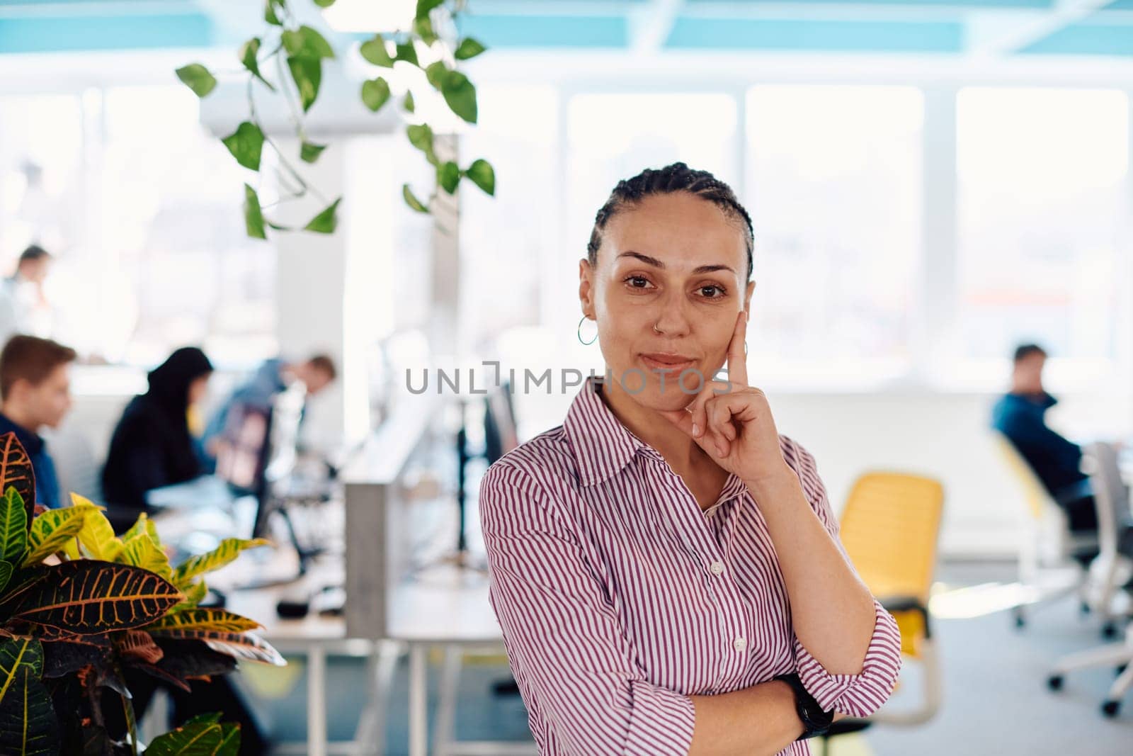 Portrait of young smiling business woman in creative open space coworking startup office. Successful businesswoman standing in office with copyspace. Coworkers working in background.