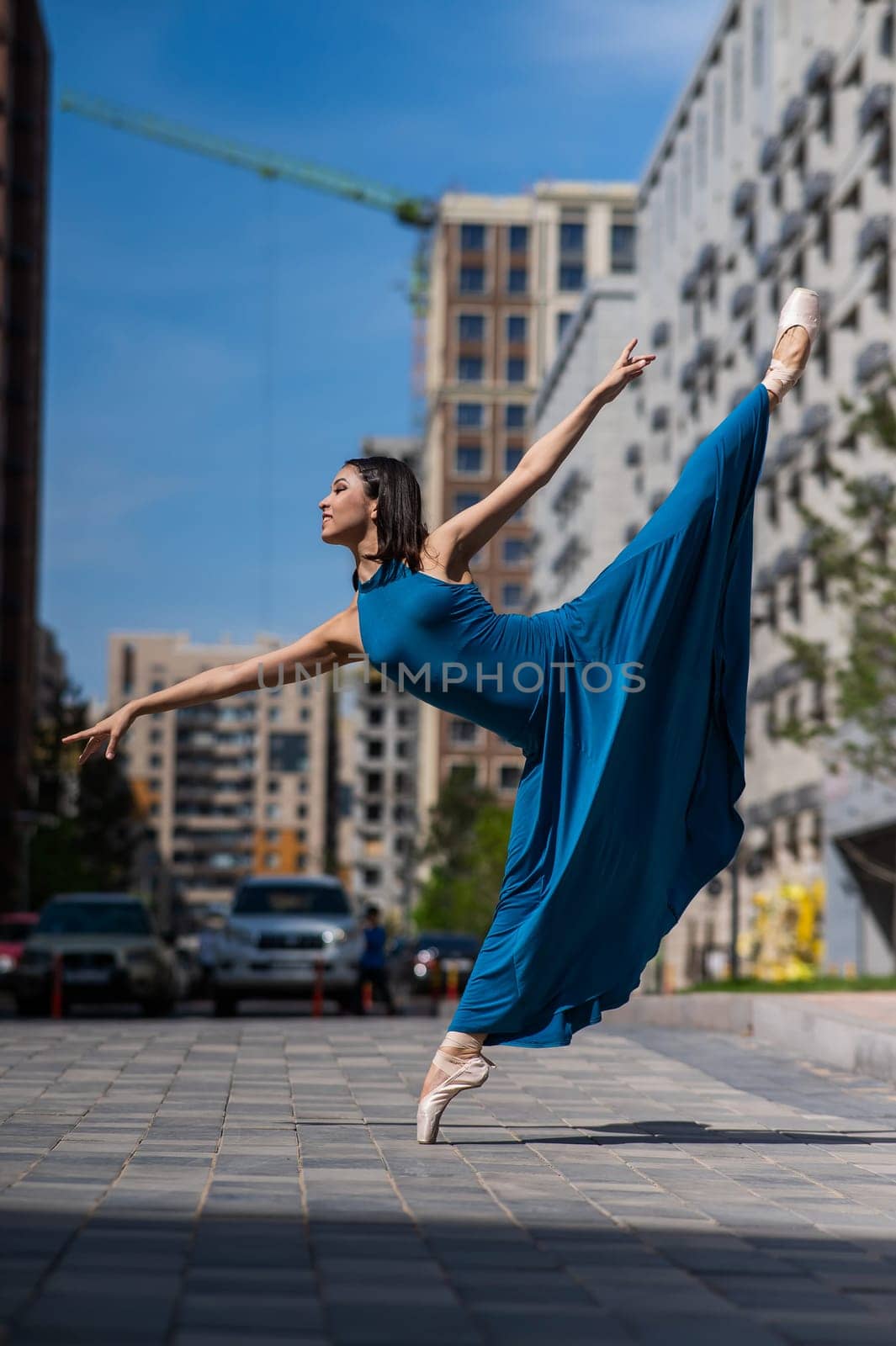 Beautiful Asian ballerina in blue dress posing in splits outdoors. Urban landscape. Vertical photo. by mrwed54