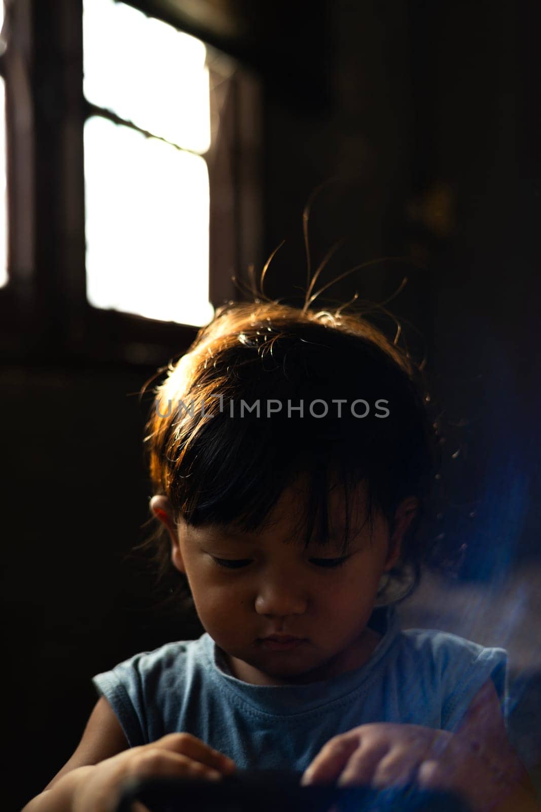 Boy sitting with his head down playing with a toy in a dark room.