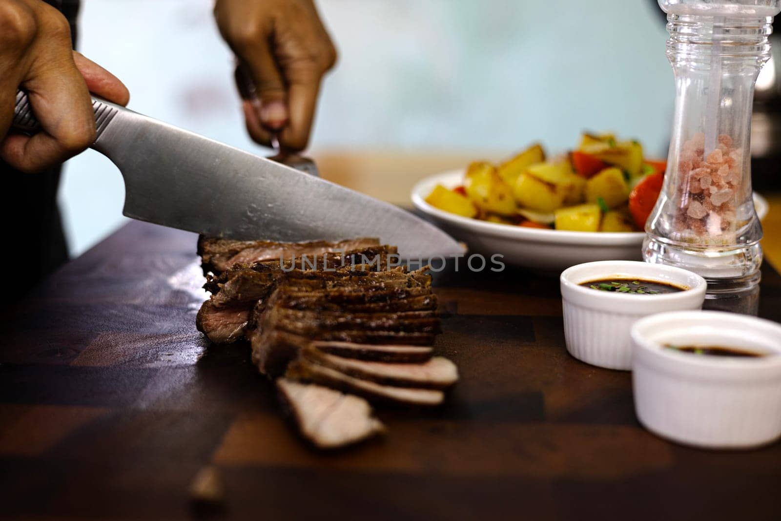 Hands cut grilled meat medium well or rib eye steak on wooden cutting board with grilled potato. close up.