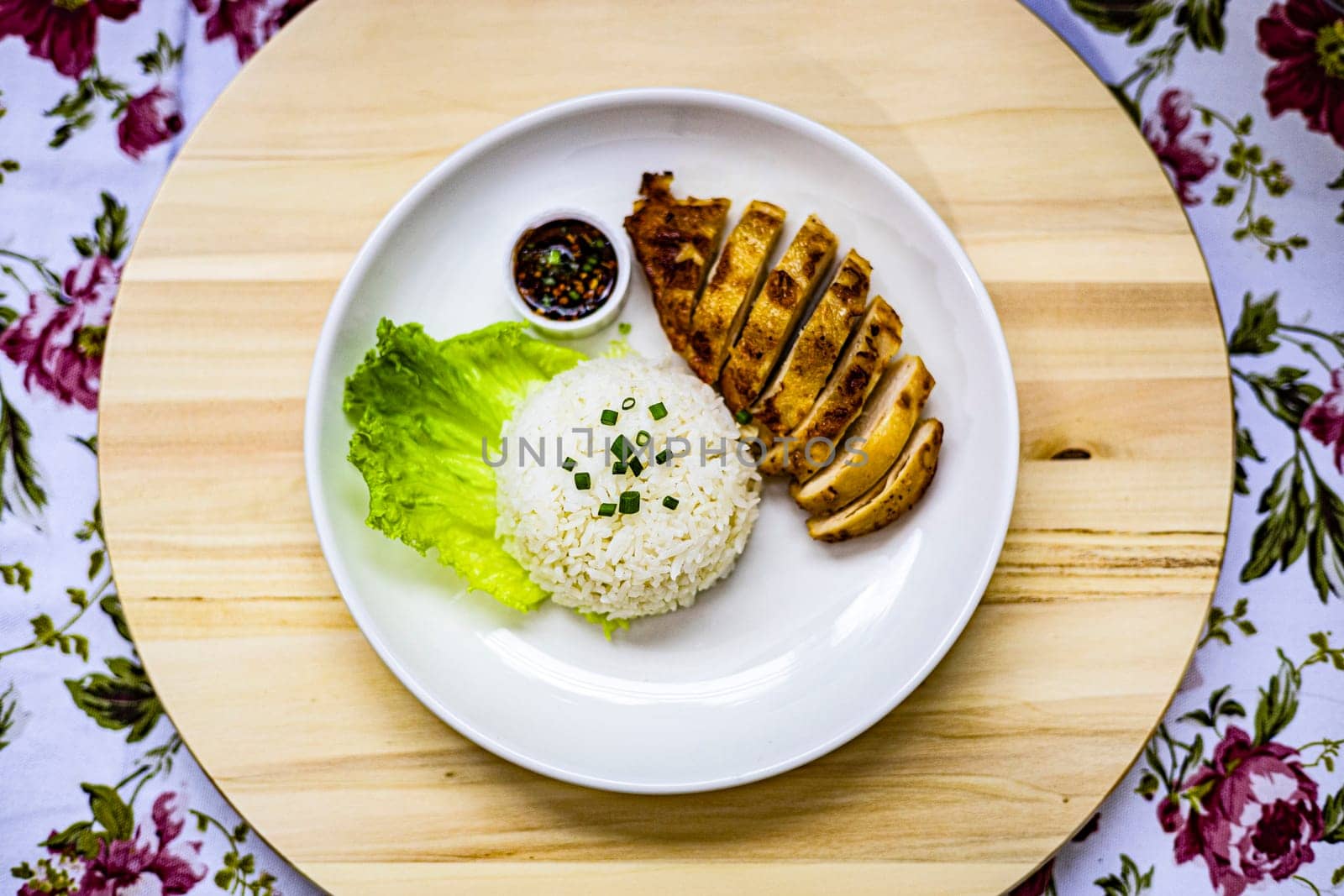 Top view of roasted chicken breast fillet steak with rice, vegetables salad and spicy sauce in white plate on wooden table. 