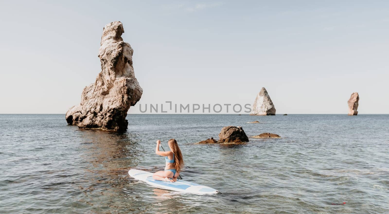 Woman sea sup. Close up portrait of happy young caucasian woman with long hair looking at camera and smiling. Cute woman portrait in a blue bikini posing on sup board in the sea by panophotograph