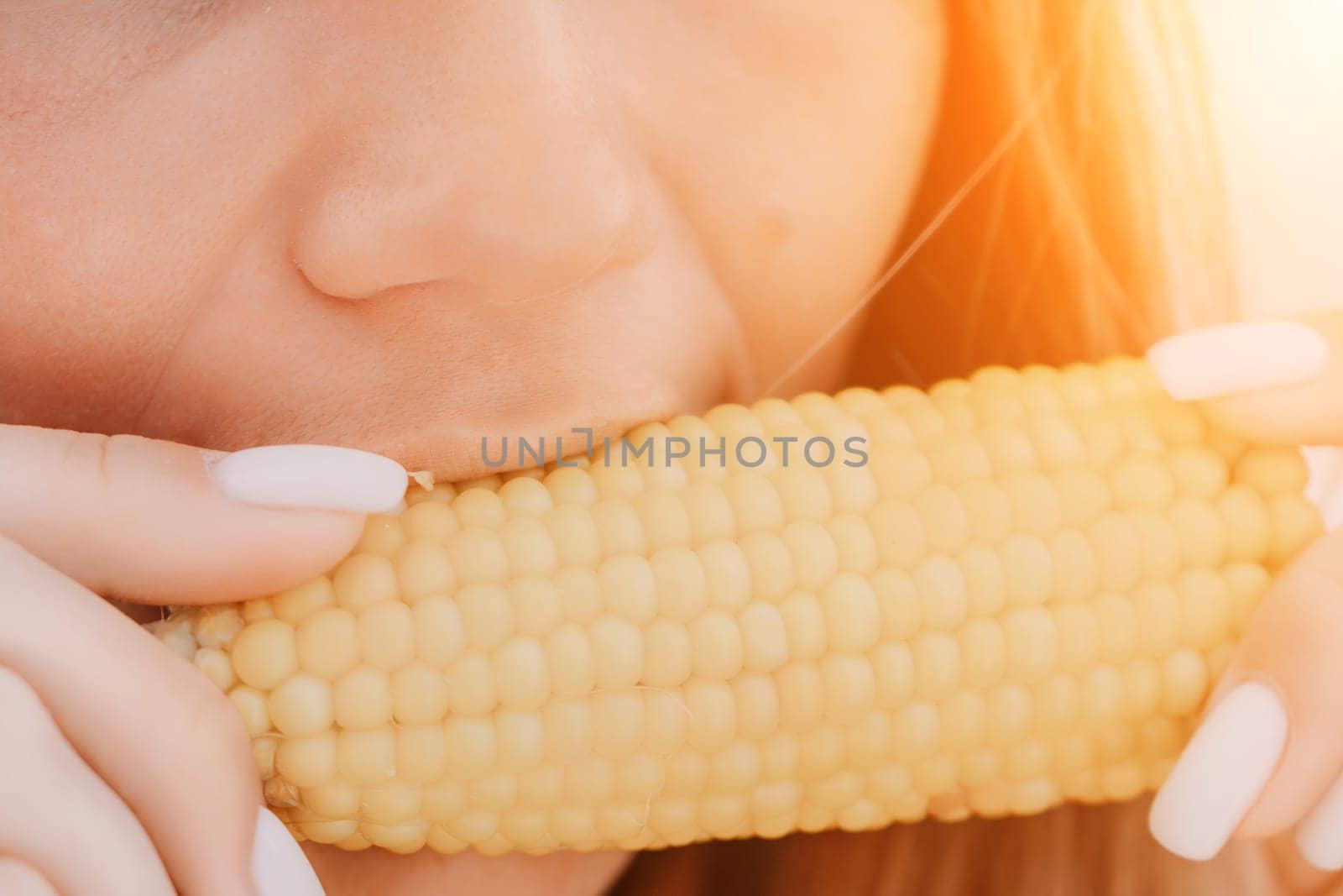 Woman eats corn on beach. Woman's hands hold delicious juicy grilled corn. A natural and healthy snack at the beach. Close-up. by panophotograph