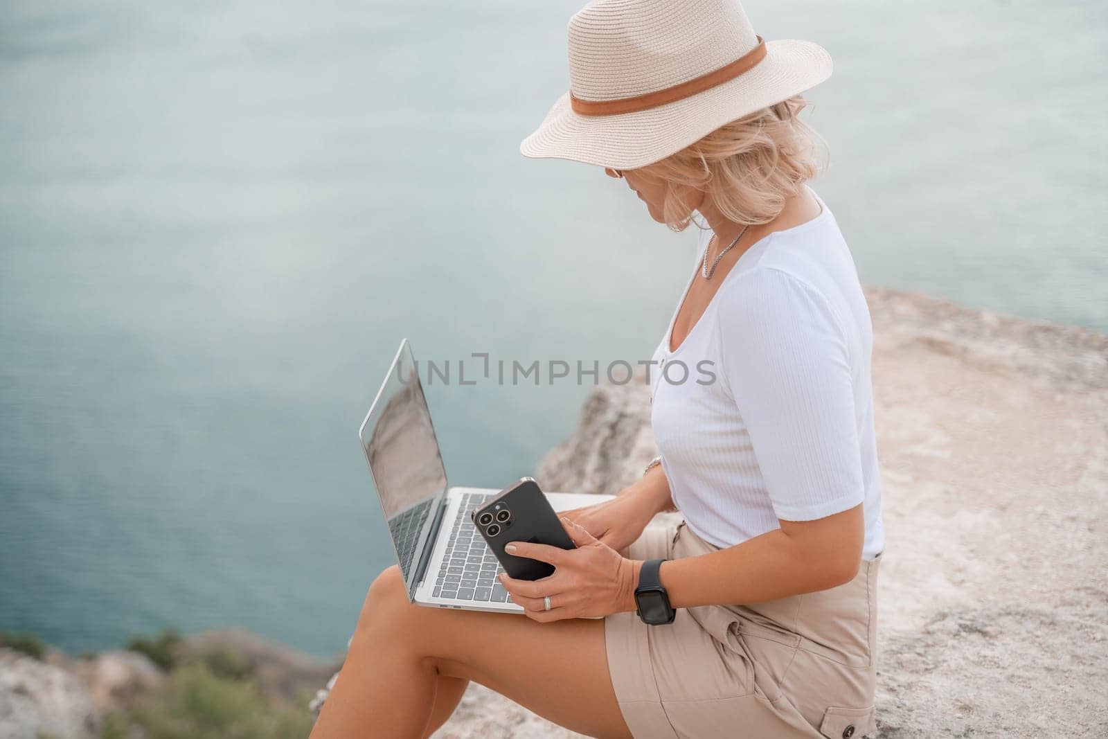 Freelance women sea working on the computer. Good looking middle aged woman typing on a laptop keyboard outdoors with a beautiful sea view. The concept of remote work