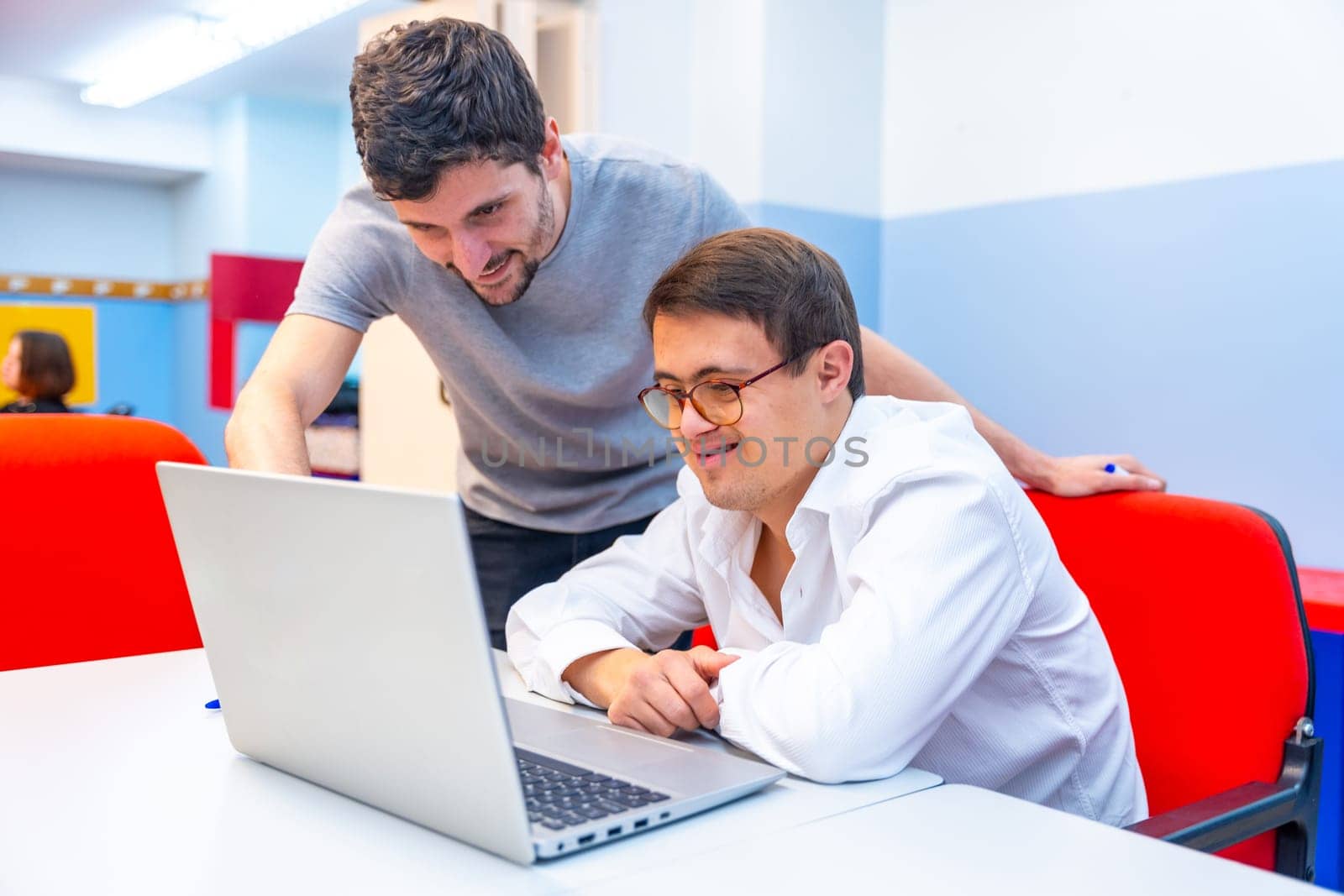 Teacher helping a man with down syndrome during computing class by Huizi