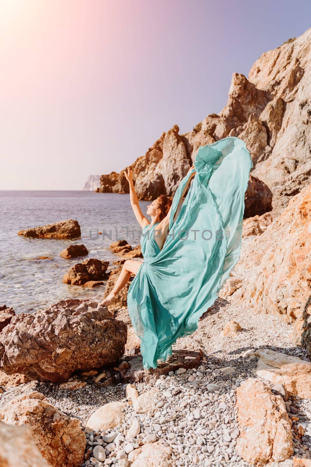 Woman green dress sea. Woman in a long mint dress posing on a beach with rocks on sunny day. Girl on the nature on blue sky background