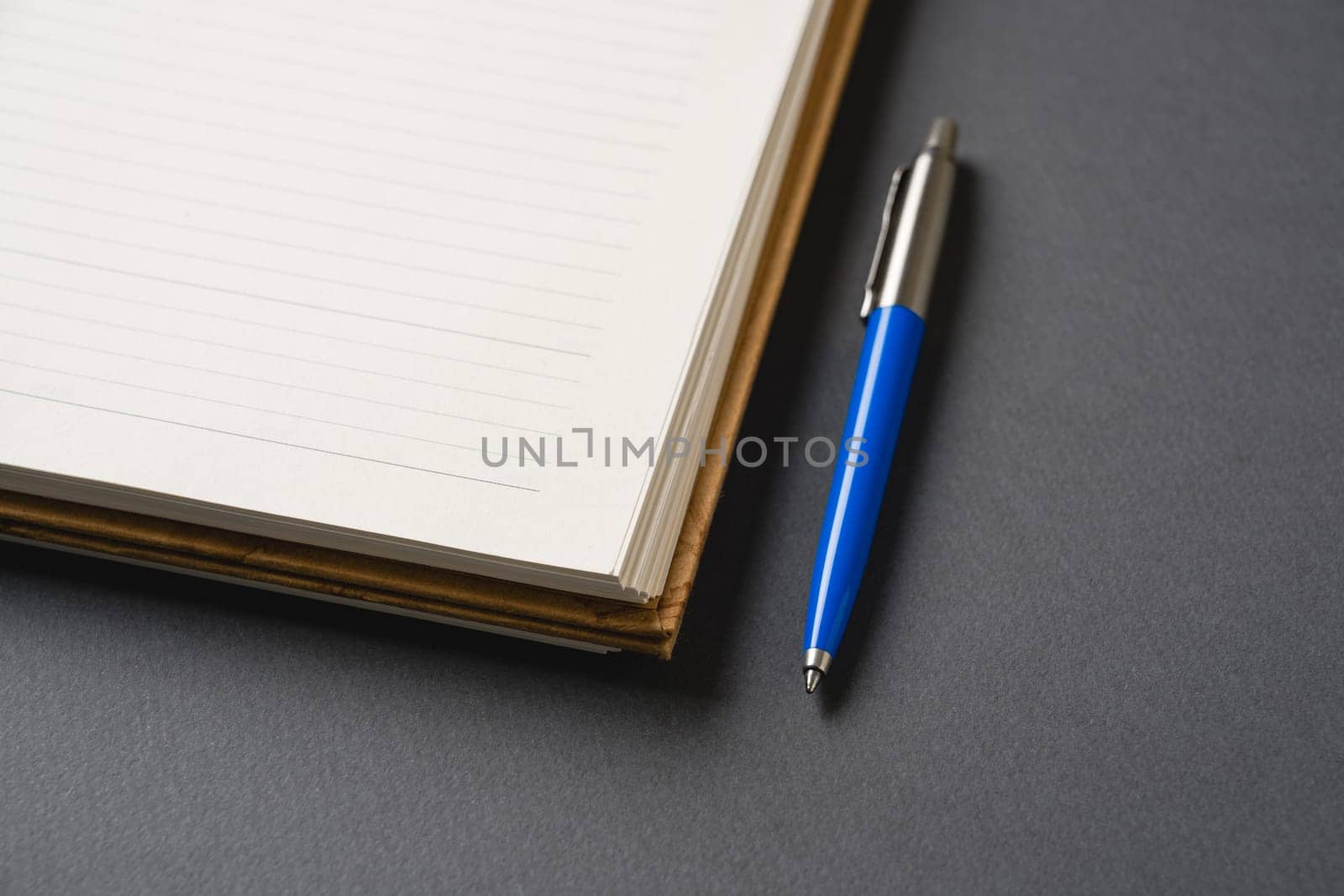 Ballpoint pen made of blue plastic and metal standing on lined notebook