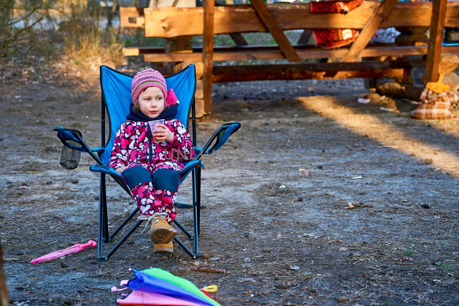 Preschool child in colorful overalls sitting in a folding chair on a picnic by jovani68