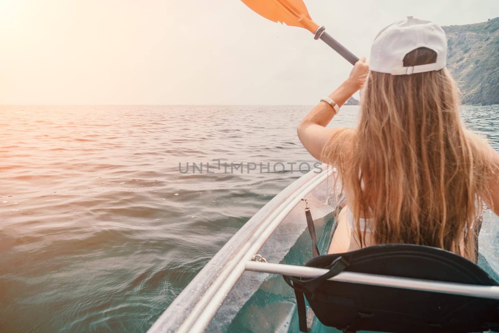 Woman in kayak back view. Happy young woman with long hair floating in transparent kayak on the crystal clear sea. Summer holiday vacation and cheerful female people having fun on the boat.