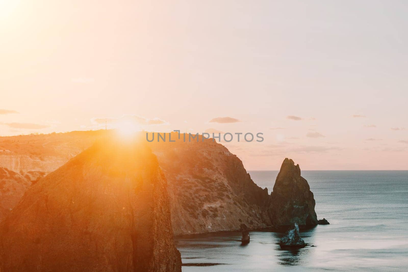 A red burning sunset over the sea with rocky volcanic cliff. Abstract nature summer ocean sea background. Small waves on golden warm water surface with bokeh lights from sun. by panophotograph