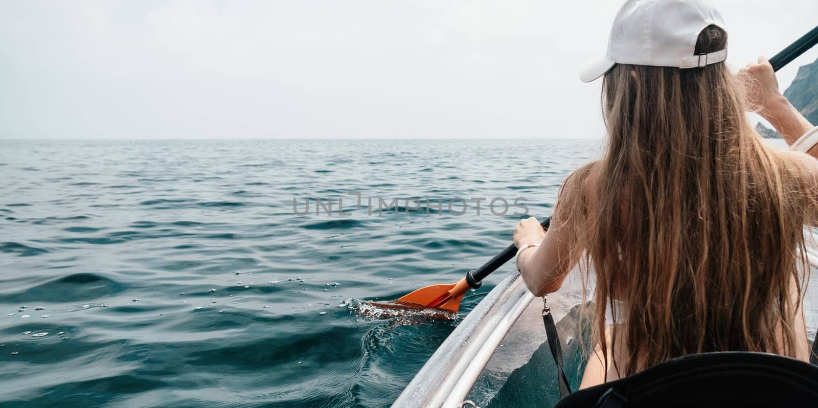 Woman in kayak back view. Happy young woman with long hair floating in transparent kayak on the crystal clear sea. Summer holiday vacation and cheerful female people having fun on the boat.