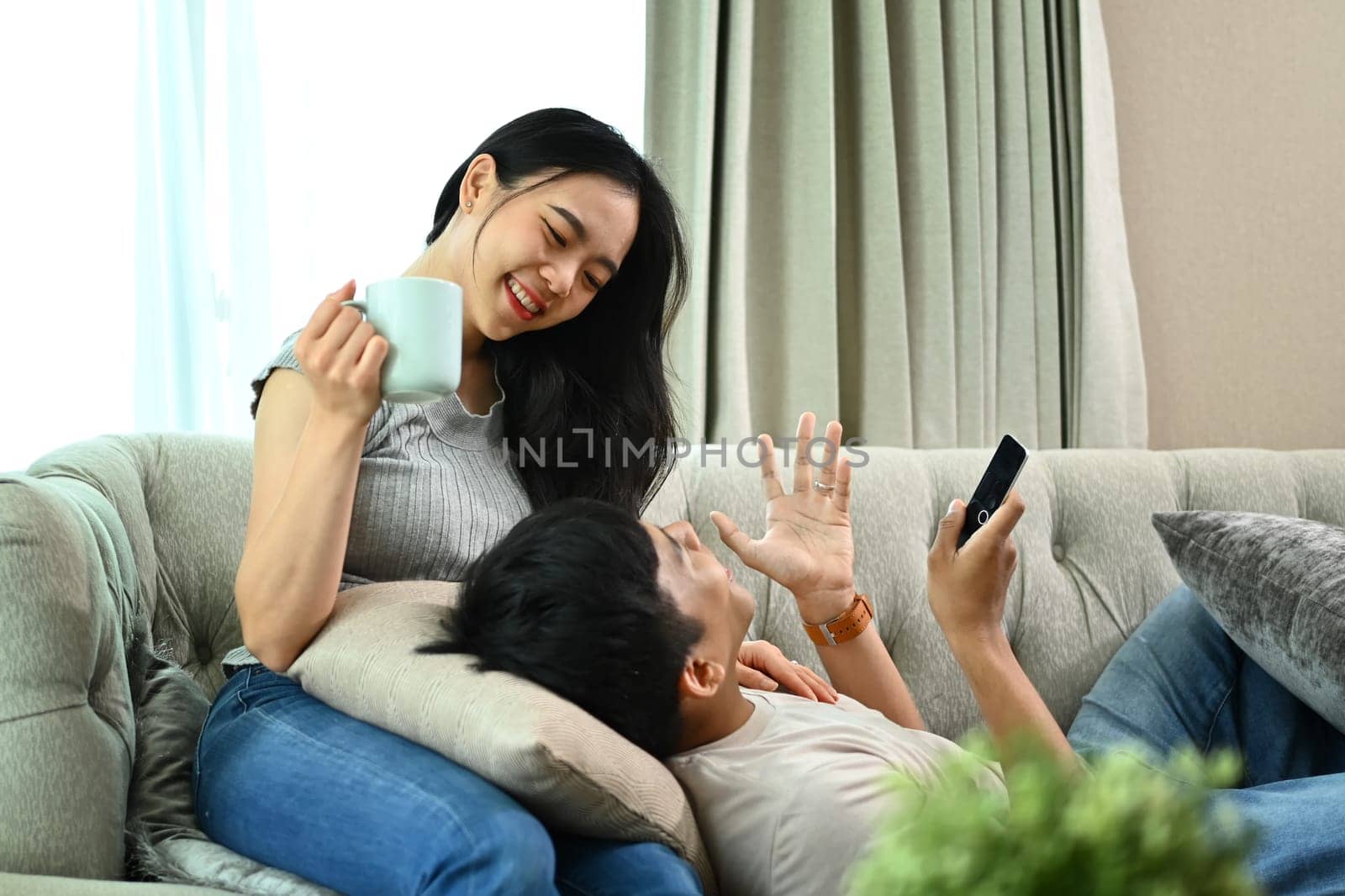 Beautiful young couple talking while watching television in cozy living room at home by prathanchorruangsak