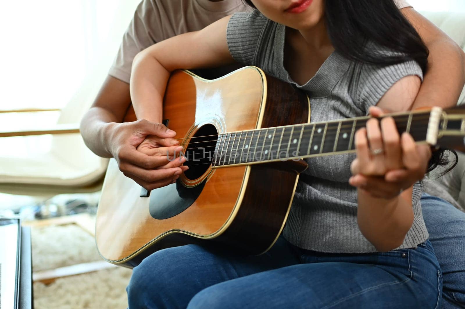 Cropped young man teaching his girlfriend playing guitar in living room by prathanchorruangsak