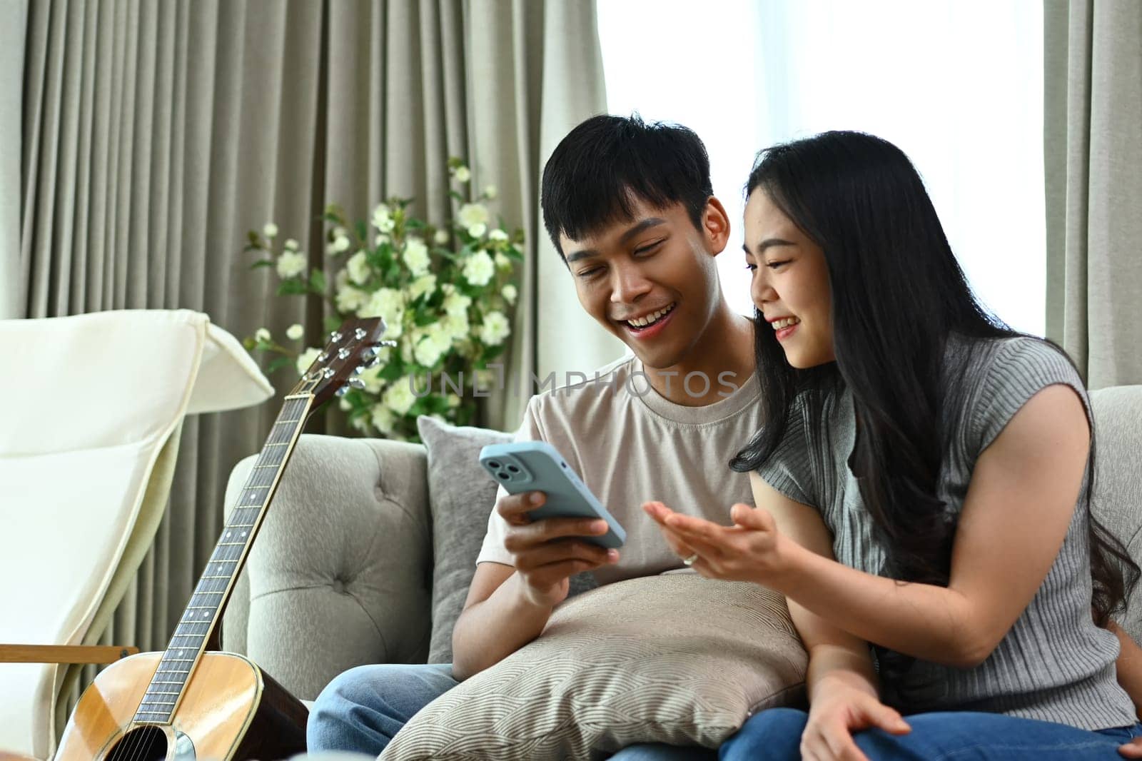 Happy young couple using mobile phone for shopping on Internet while sitting on couch.