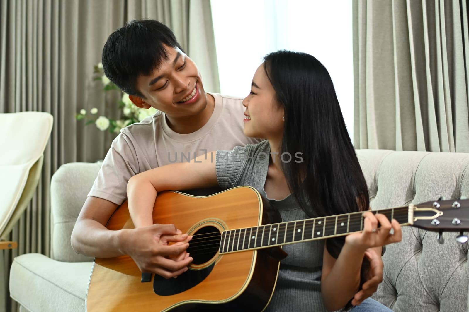 Affectionate Asian couple playing guitar while relaxing on weekend at home by prathanchorruangsak
