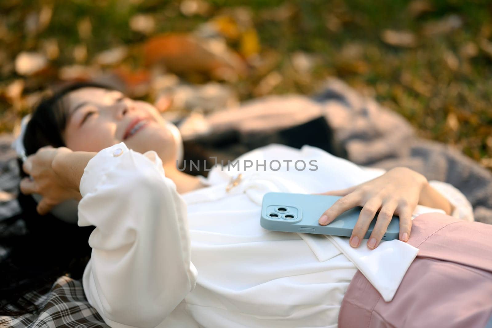 Pleased female office employee listening to music and enjoying fresh air, lying checkered blanket by prathanchorruangsak