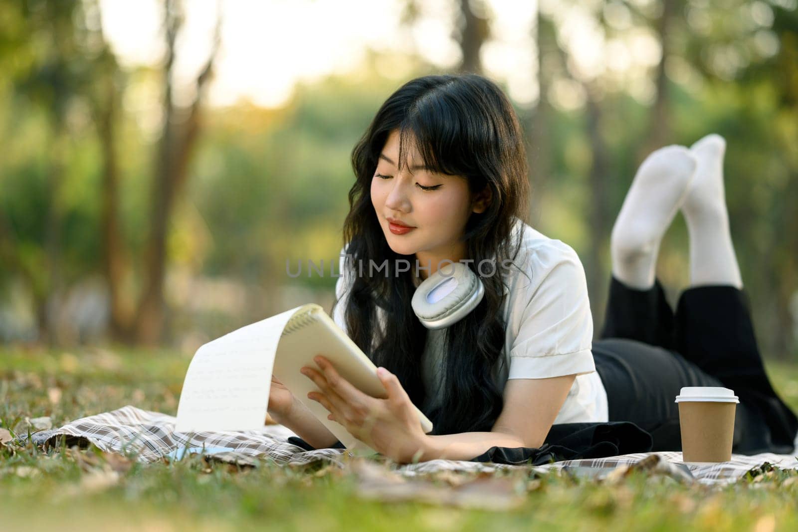 Peaceful young woman relaxing on green grass and reading book.
