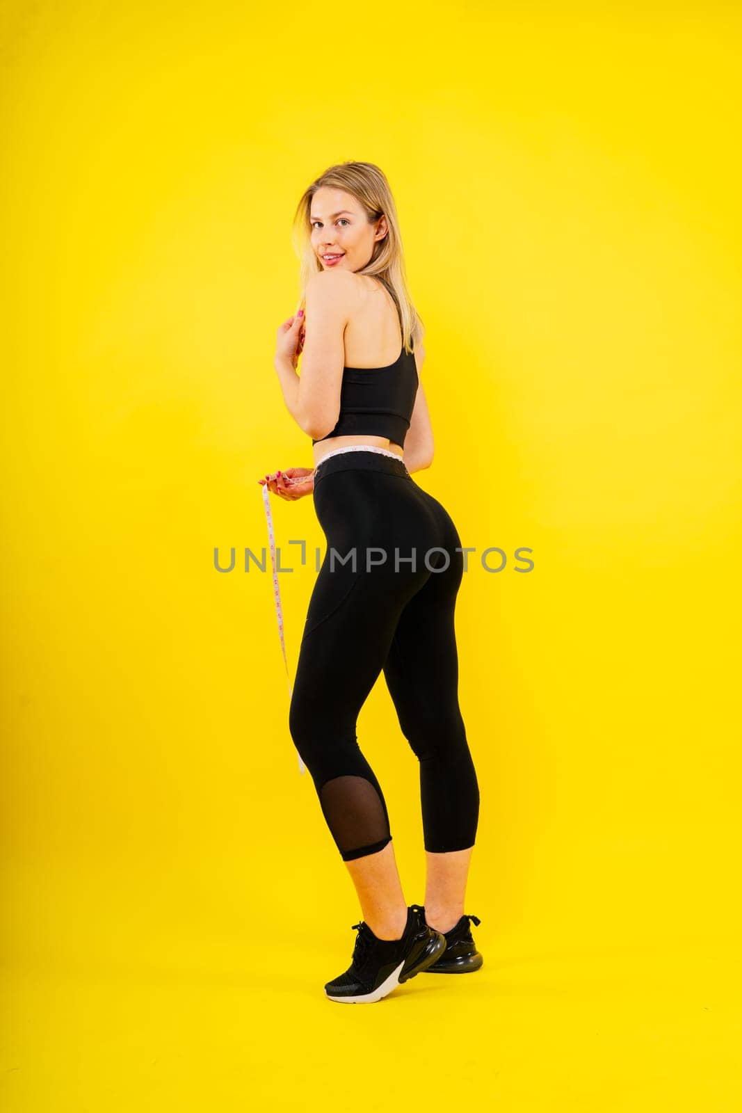 Smiling slim woman measuring her waist with tape. Fit young lady perfect shape, happy her body