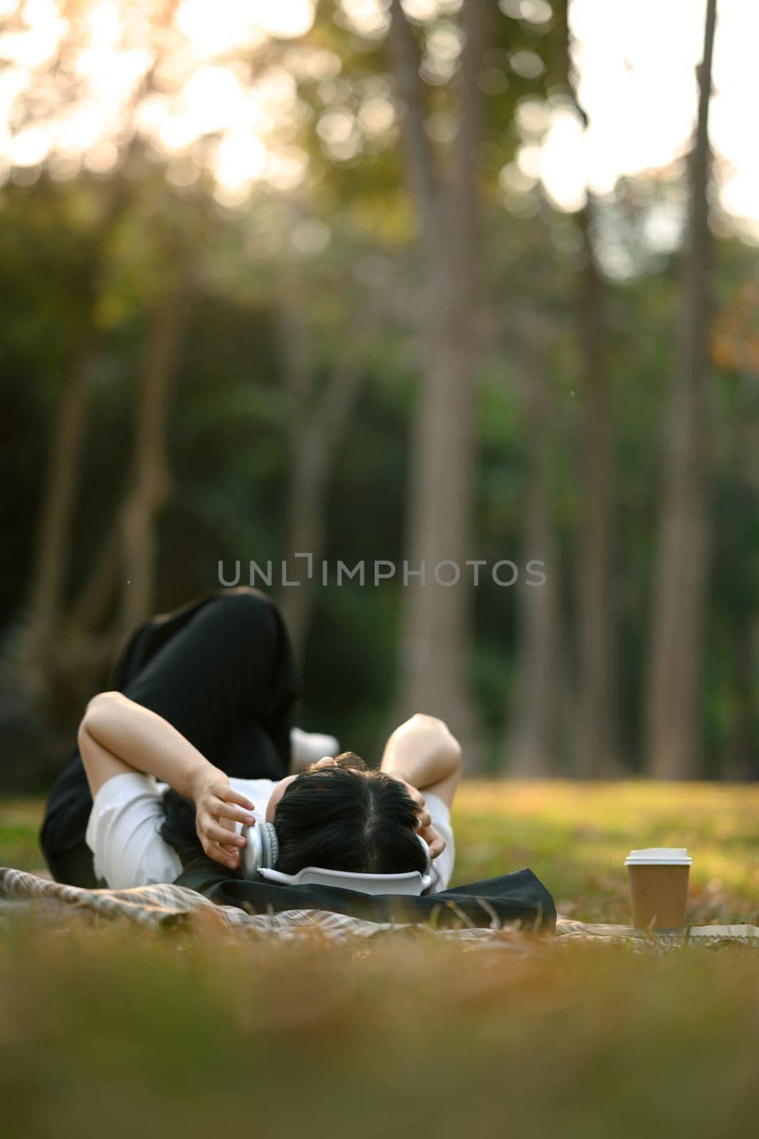 Relaxed young woman lying on lawn and listening music in headphone.