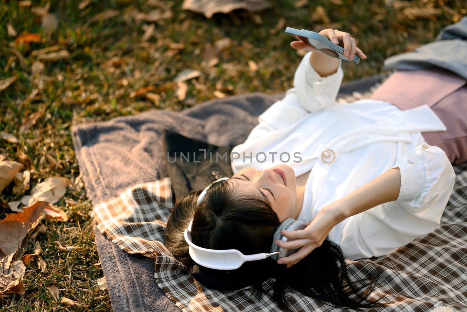 Happy asian business woman chilling in the park and listening to music with headphone.