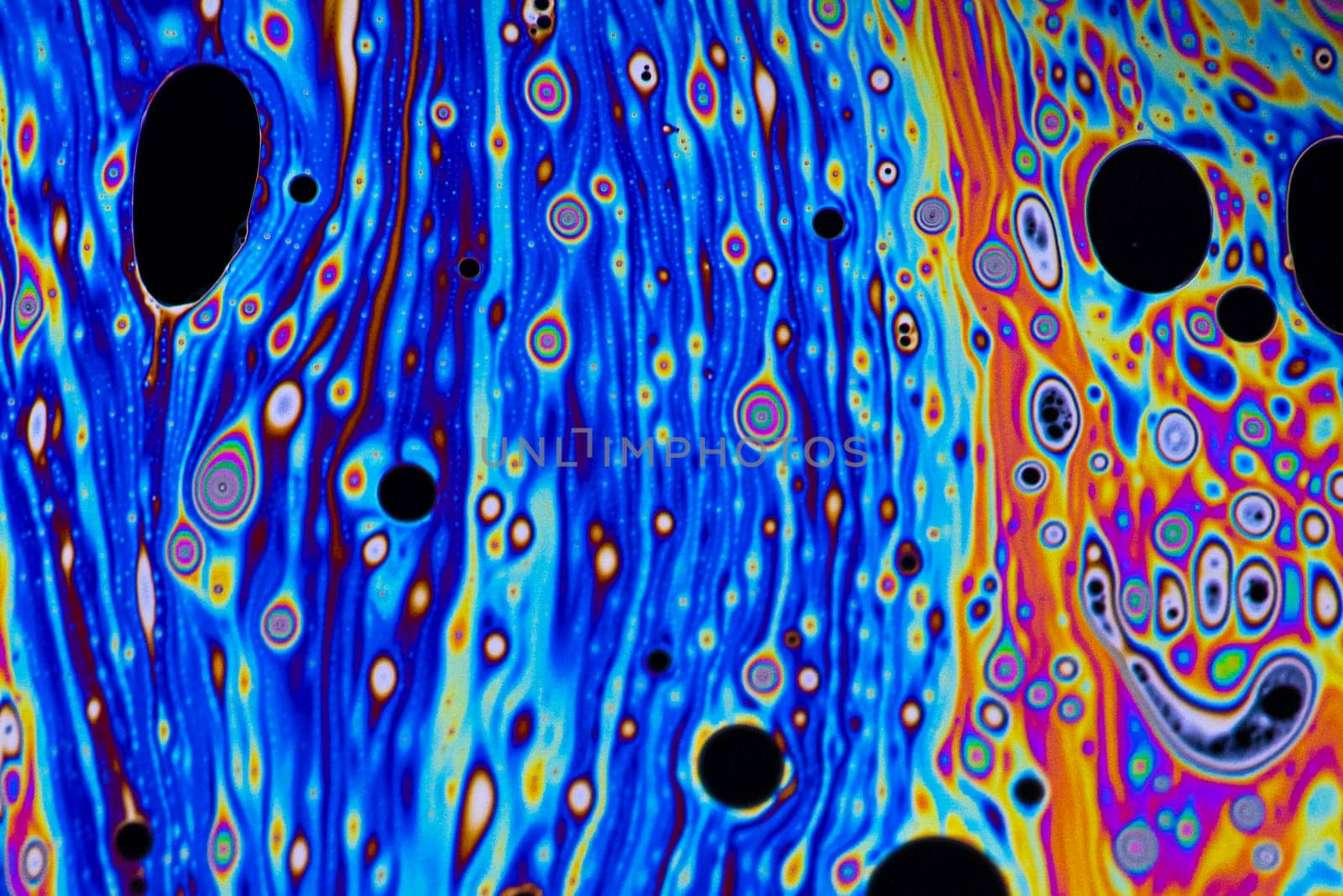 Bright blue, pink, purple, and orange pastel colours swirl around intense black and white dots patterns on the surface of a soap bubble.