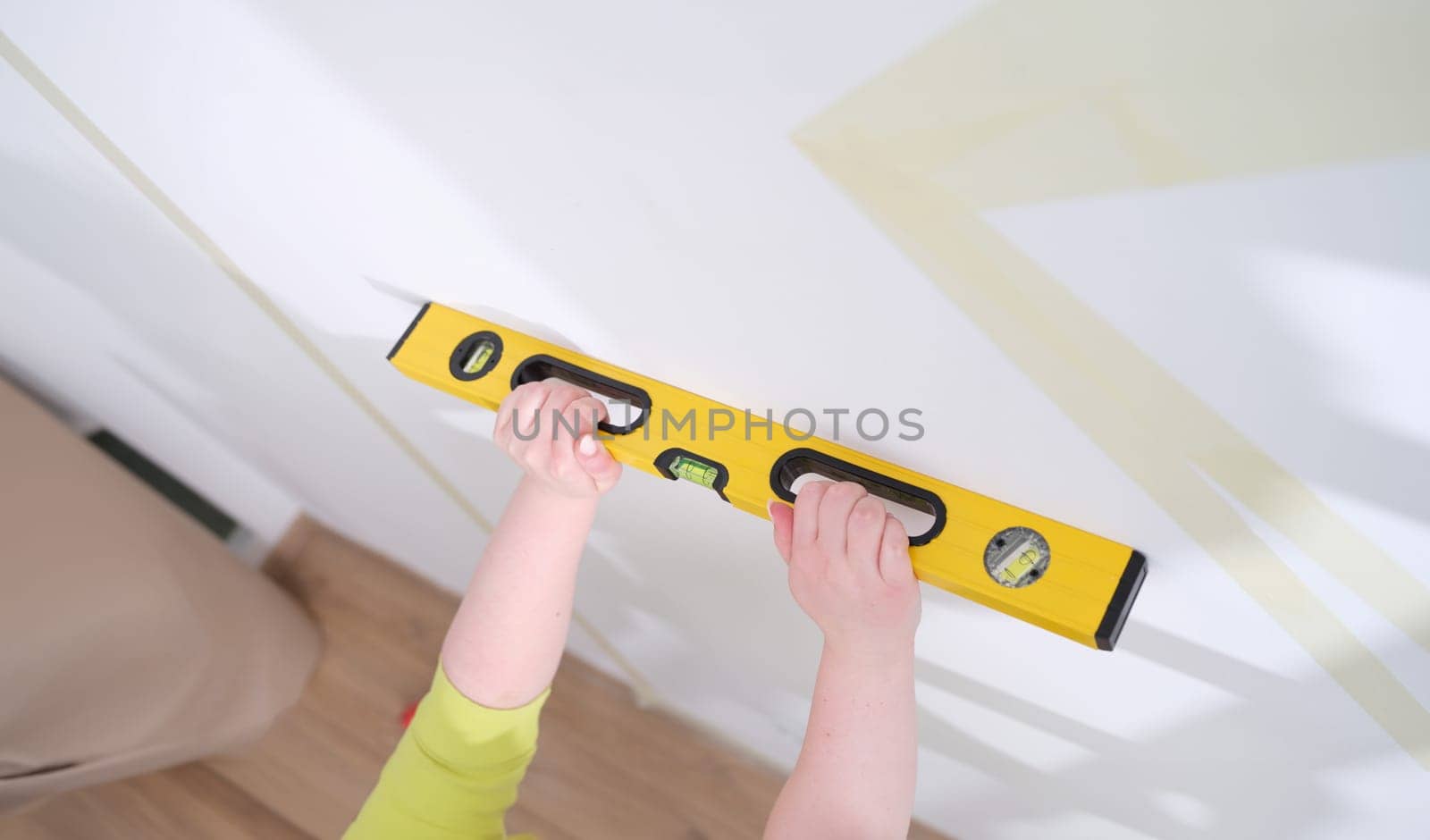 Hands of worker hold yellow level against white wall. Home craftsman and the evenness of walls concept