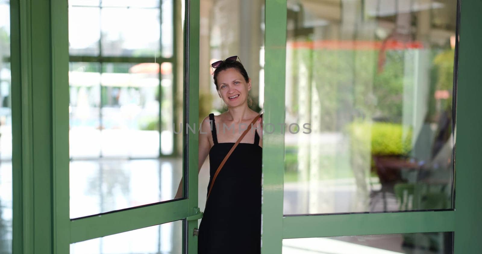 Smiling young woman opening front door to hotel house and shop. Welcome and hospitality concept