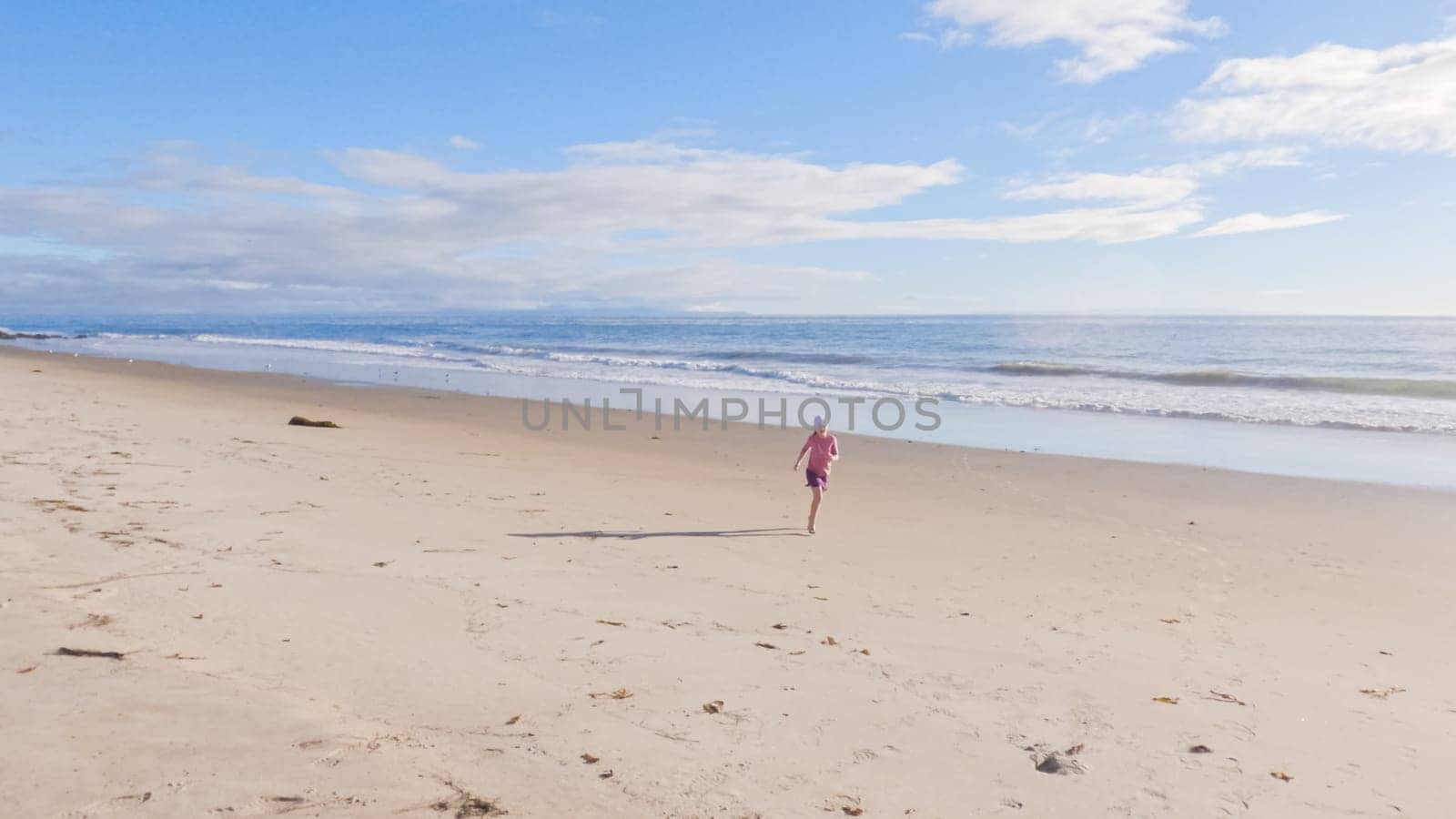 A little girl joyfully plays on the vast, empty sands of El Capitan State Beach in California during winter.