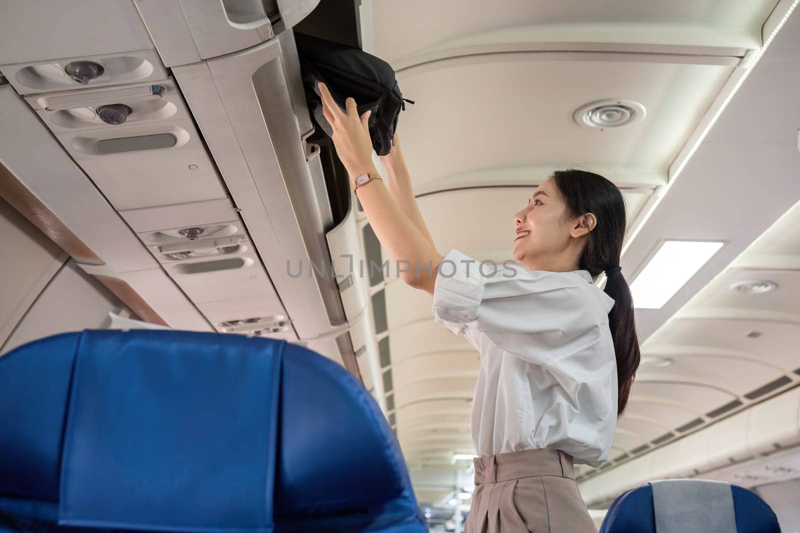Young woman traveling by plane put her bag in the luggage compartment of the plane. by wichayada