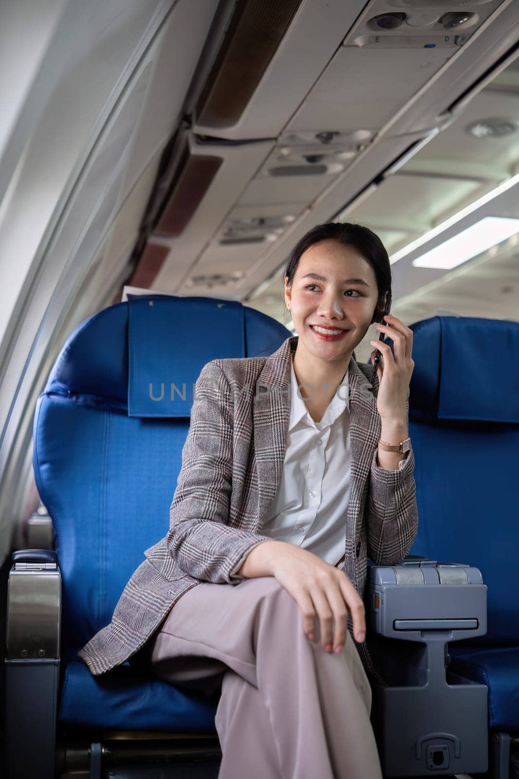 Young woman talking on the phone, communicating on business before traveling Sitting near window in first class on airplane during flight, travel and business concept. by wichayada
