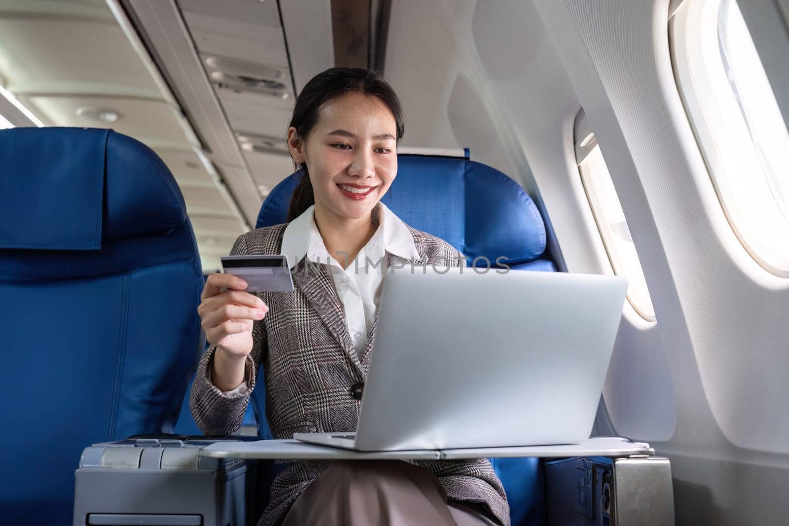 Young Asian woman holding credit card shopping online using website on laptop Sitting near window in first class on airplane during flight, travel and business concept..