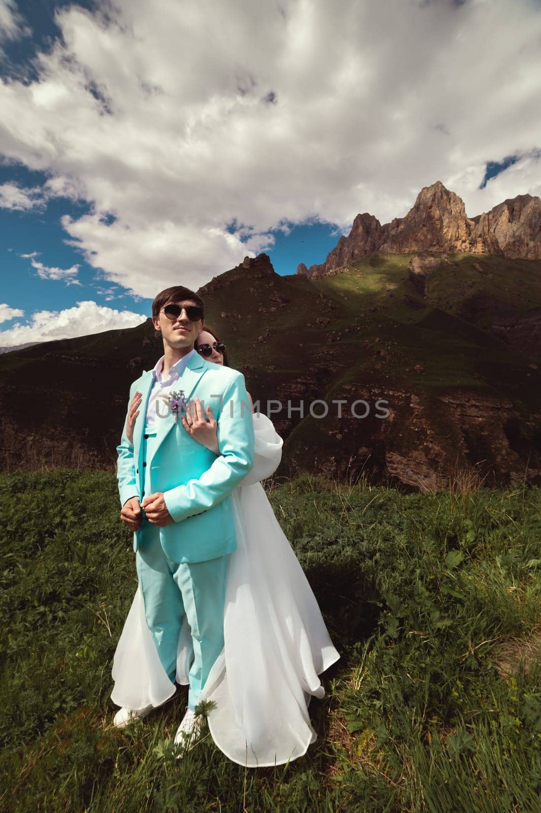 A young man and his wife stand in an embrace high in the mountains against the backdrop of epic rocks on a sunny day. Newlyweds wedding couple in the mountains by yanik88