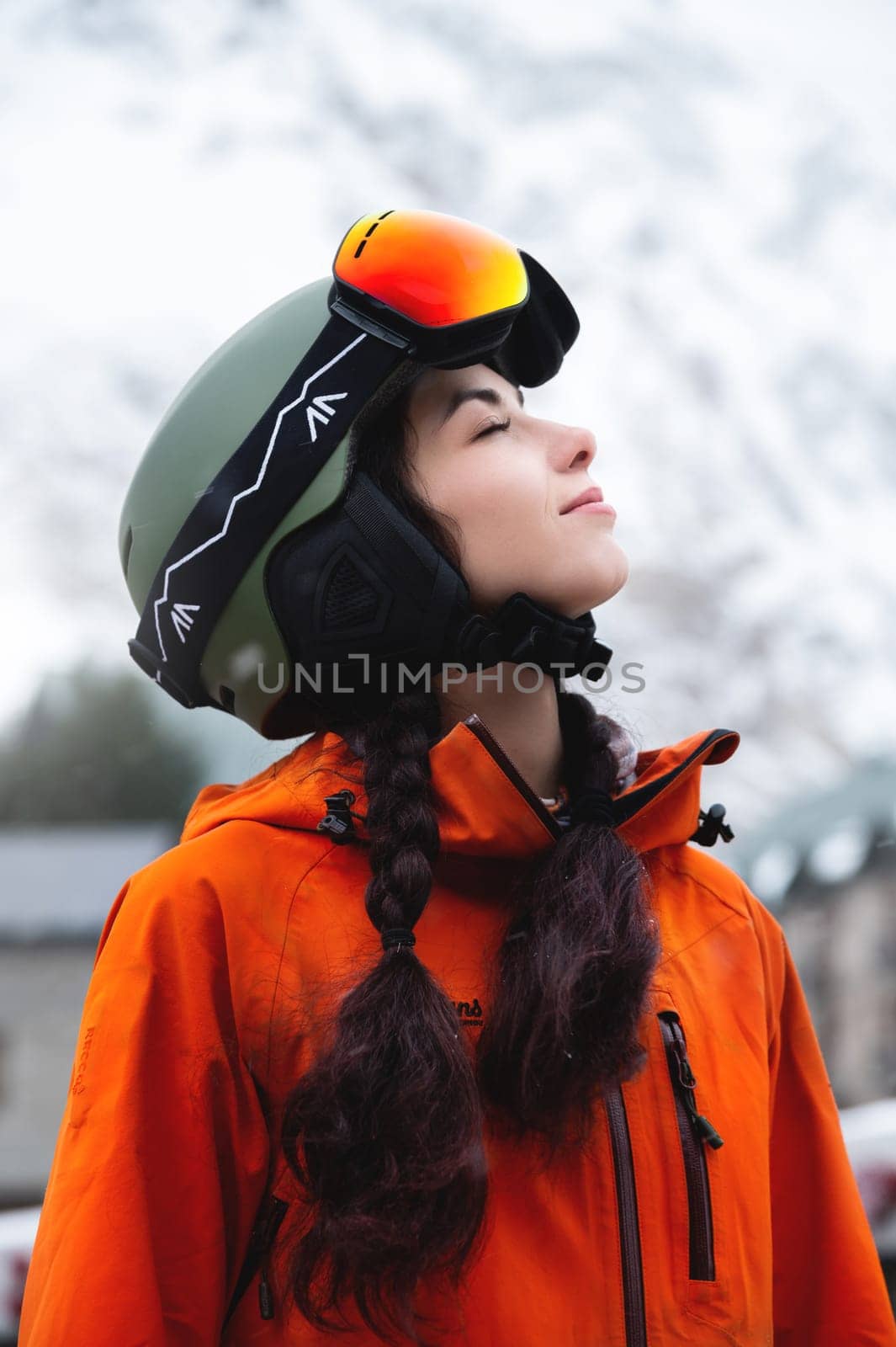 young woman of Caucasian ethnicity looks to the side and smiles, raising her head to the sky, enjoying her vacation at the ski resort by yanik88