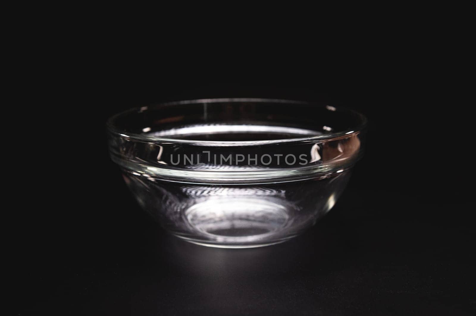 Empty glass plate or salad bowl for one person, on a black background, close-up.
