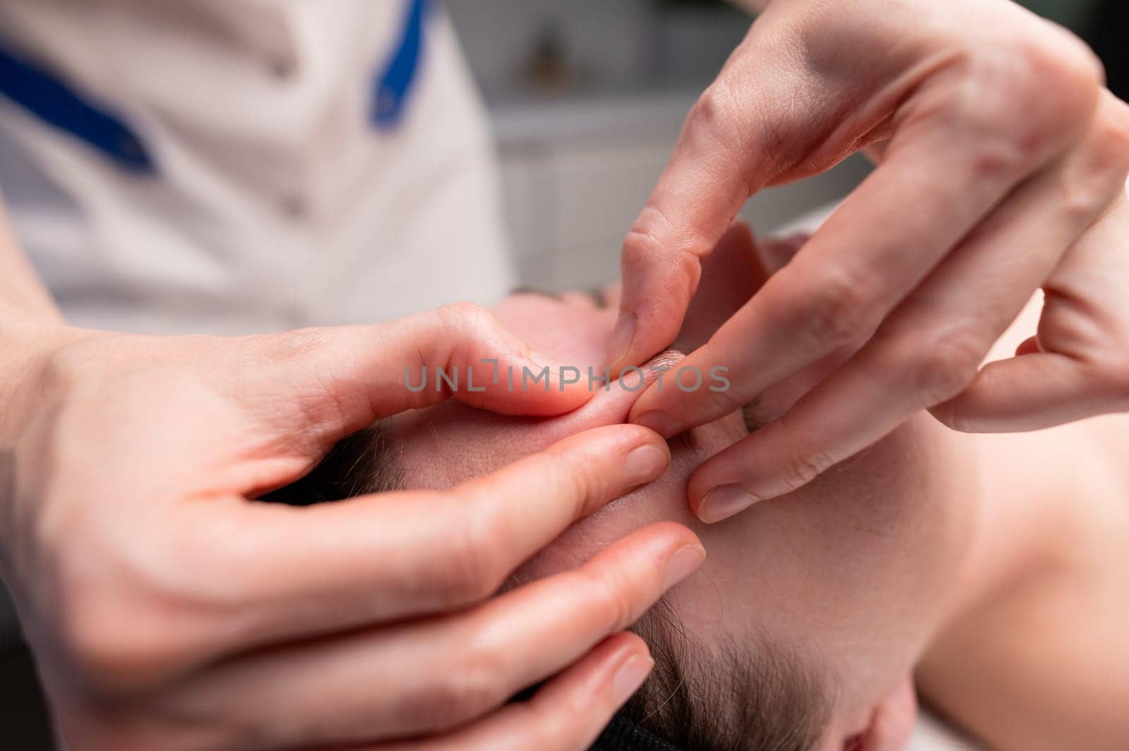 Close-up shot of a woman's head doing a facial massage on a treatment table. Therapist applying pressure with thumbs on forehead by yanik88