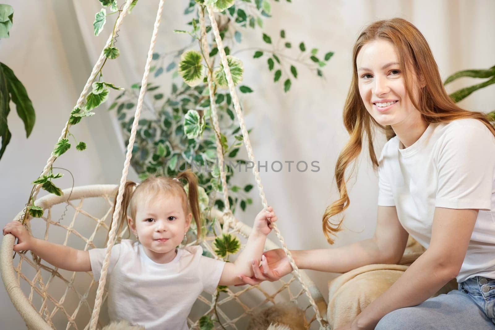 Happy loving family. Mother and daughter child girl playing and hugging in living room with wicker chair