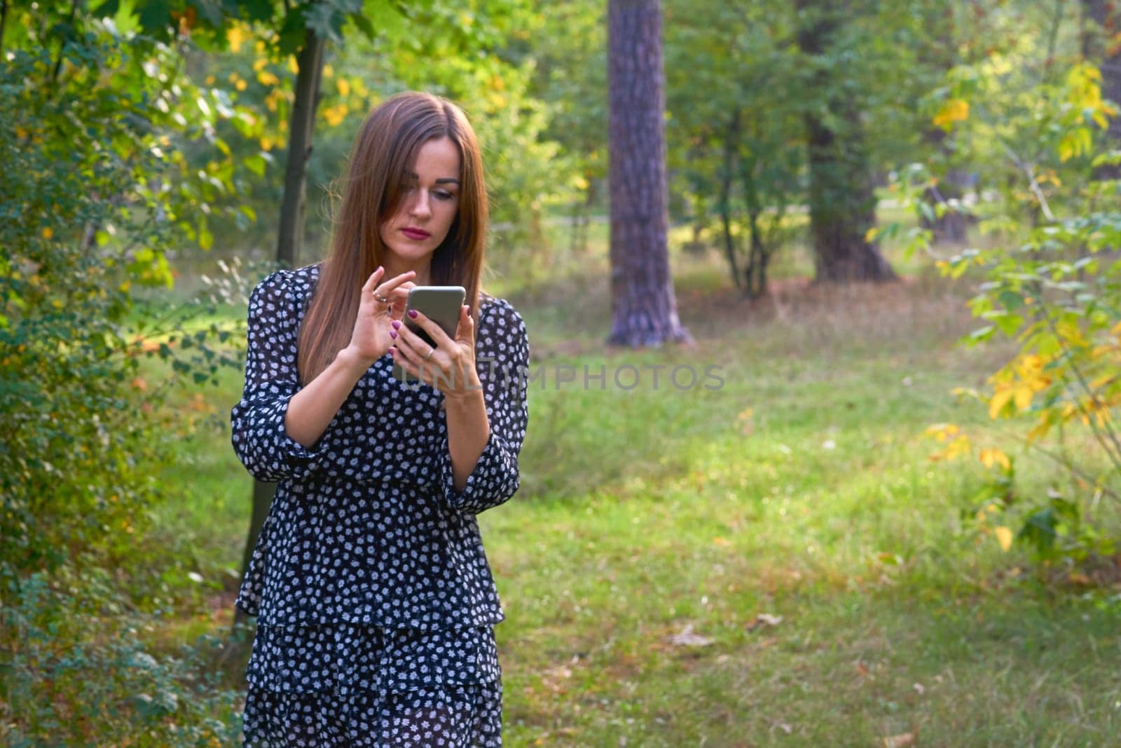 Pretty woman writes a message, looks at the phone, trees in a forest park by jovani68