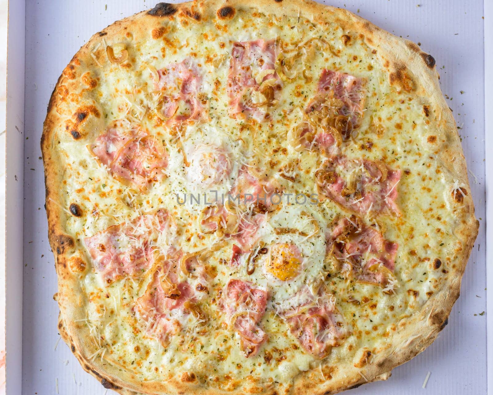 Fresh pizza carbonara with ham and scrambled egg on the concrete background,