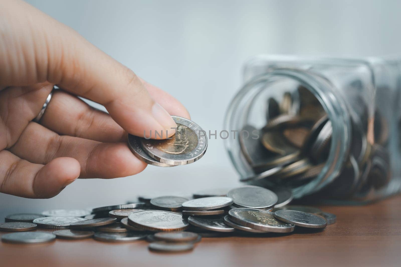 Coins spilling out of a glass jar with hand. Saving money concept. by iamnoonmai