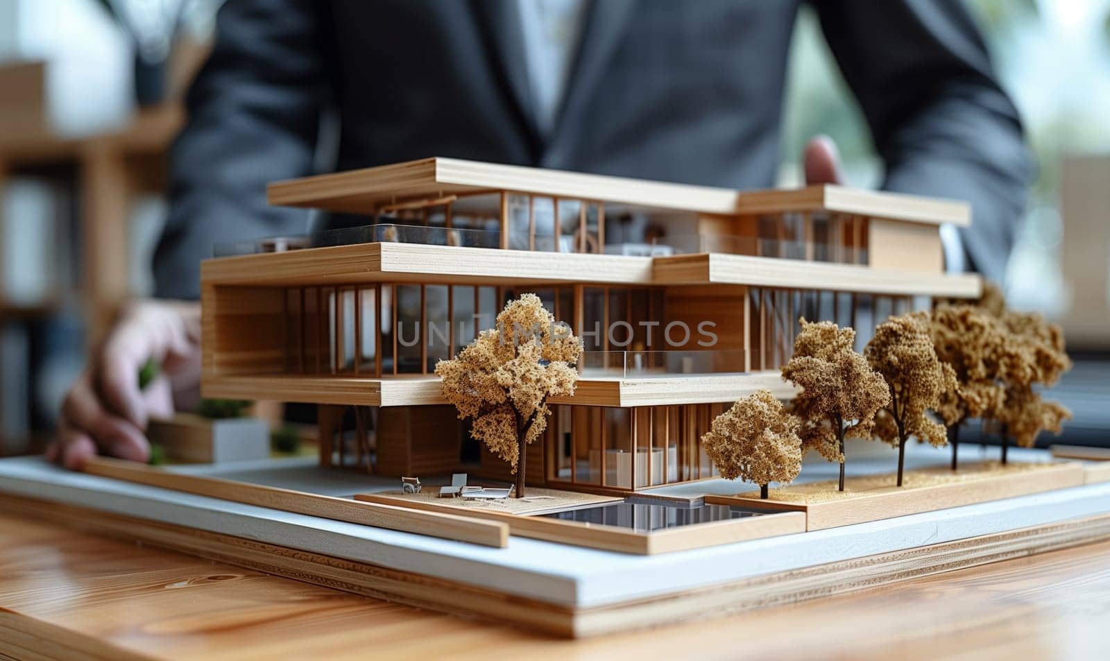 A man is showcasing a miniature wooden house model on a table, highlighting the intricate hardwood facade, roof, and flooring details